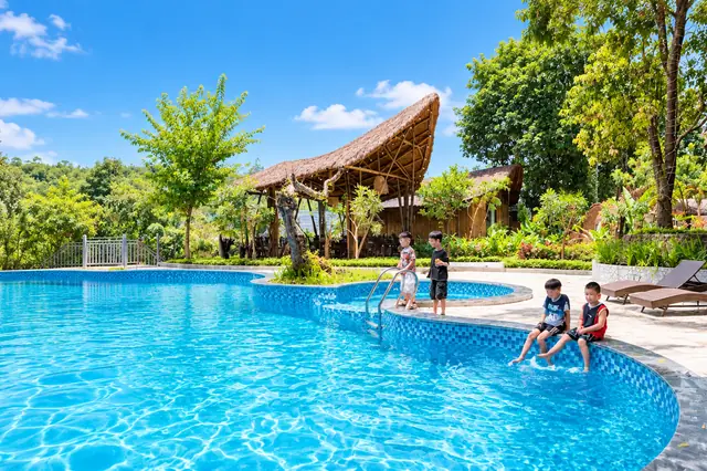 Chòi tre mái tranh cong bên bể bơi giữa vườn, mấy bạn nhỏ ngồi ngâm chân ở mép bể